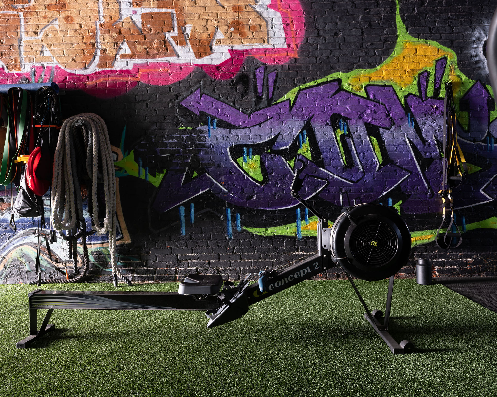 Rowing machine and battle ropes in front of a graffiti wall at The Gym Philly