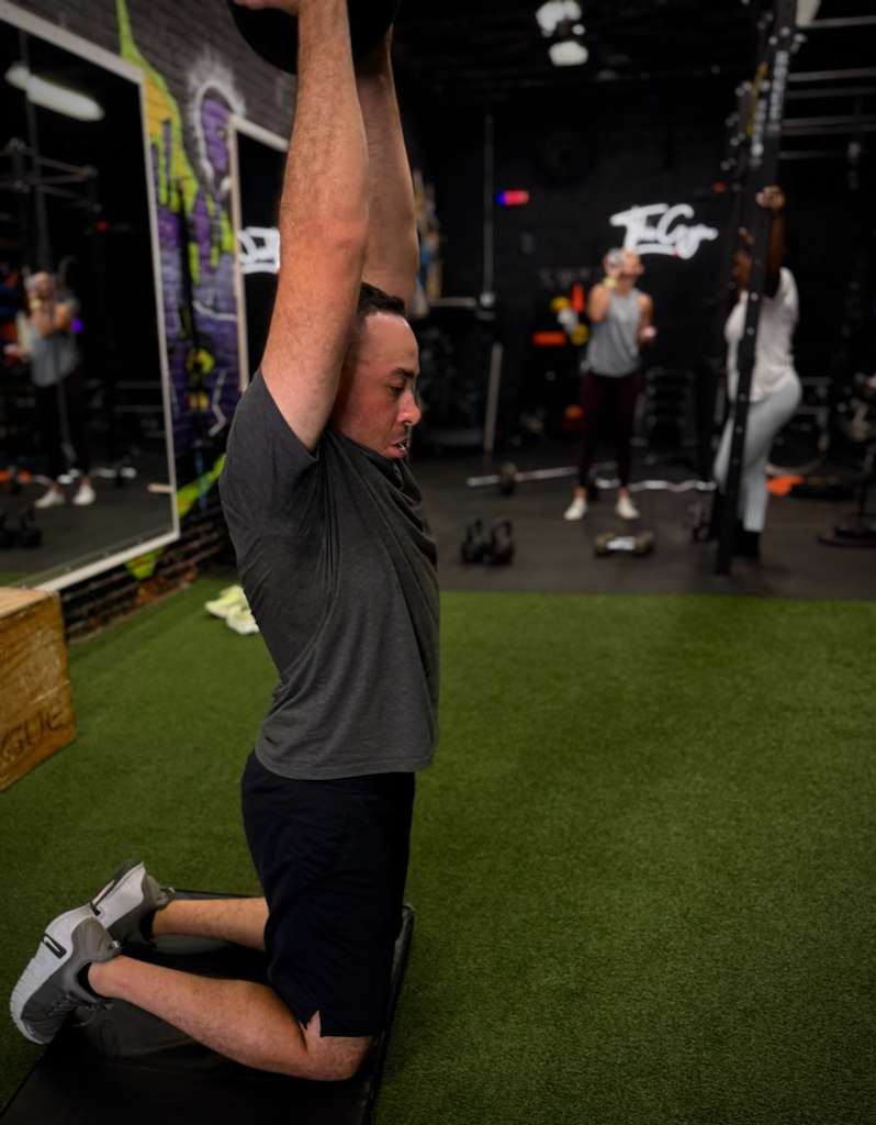 Client in a tall-kneeling overhead stretch on the turf