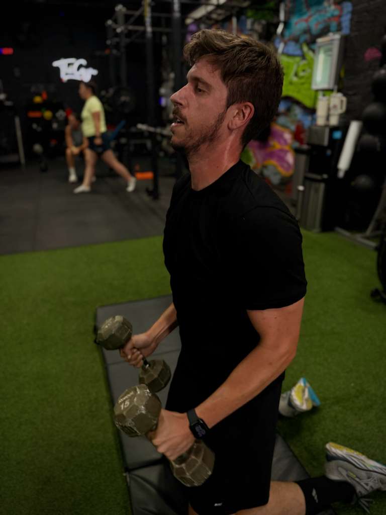 Client holding dumbbells in a split squat on the gym turf