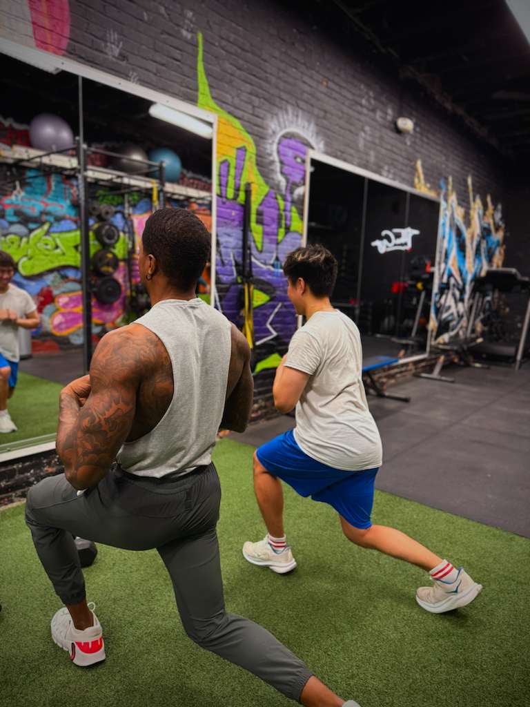 Coach and client doing reverse lunges together on the turf