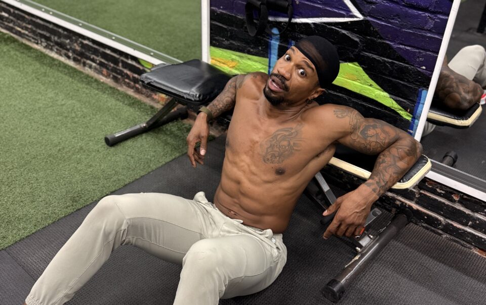 Brandon RaSean seated on the gym floor beside a dumbbell at The Gym Philly.