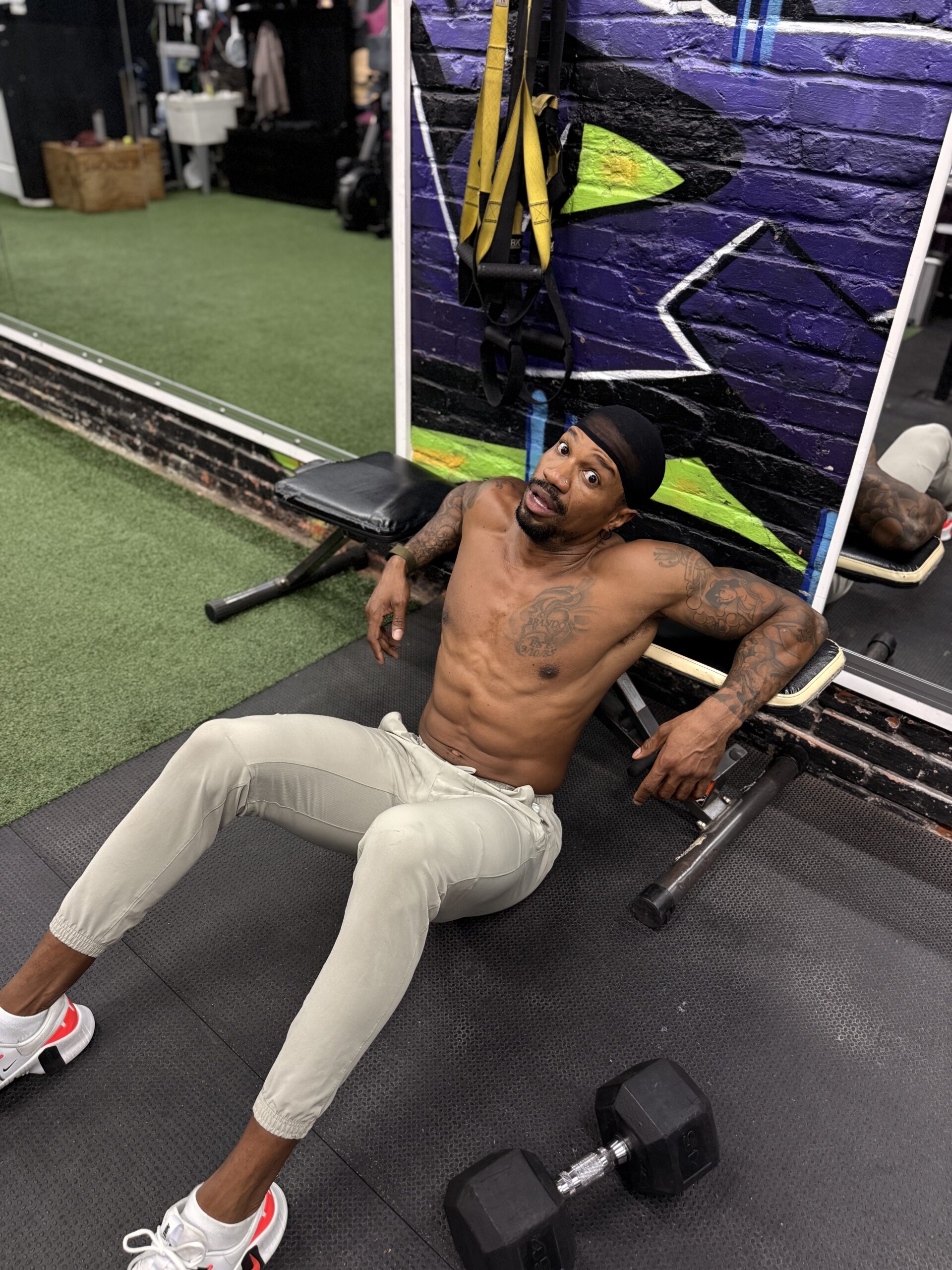 Brandon RaSean seated on the gym floor beside a dumbbell at The Gym Philly.