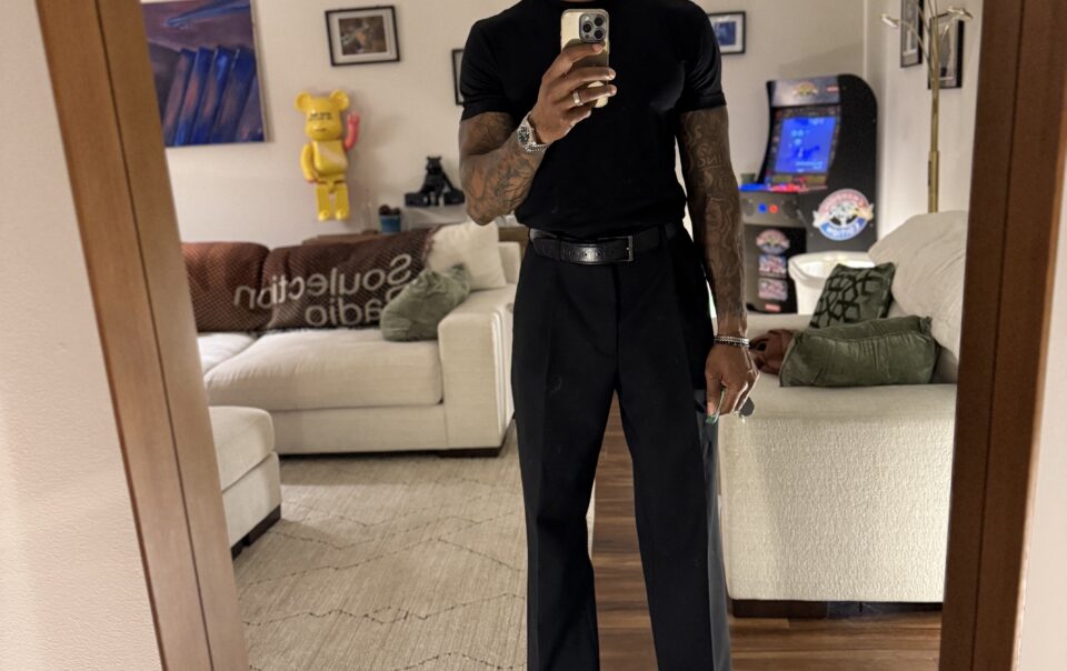 Brandon RaSean wearing a fitted black T-shirt, wide-leg black trousers, a belt, and black boots.